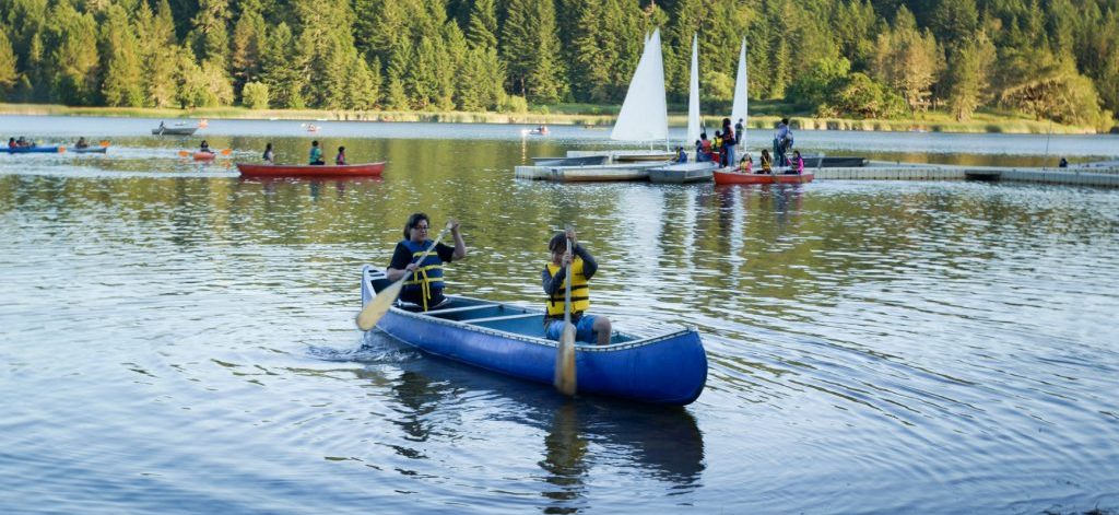 Campers paddling up to shore in a blue canoe at Waterfront.