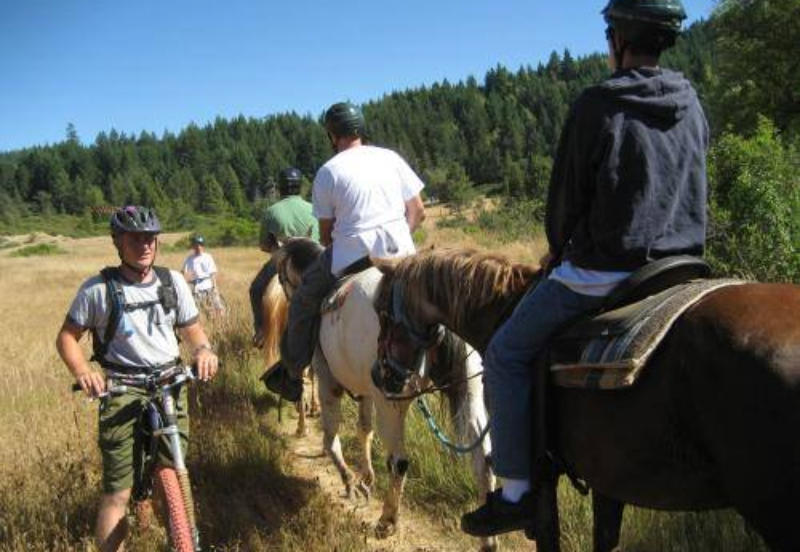 Mountain bikers observing trail right of way and pausing off to the side as the Risin' W Corral trail ride comes through.