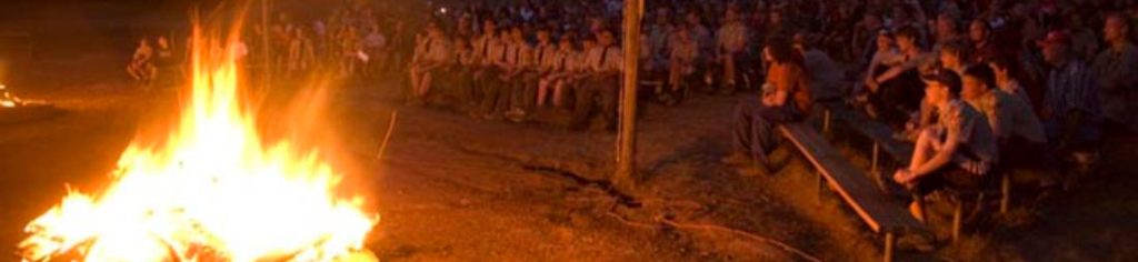 Scouts BSA campers in uniform enjoying campfire.